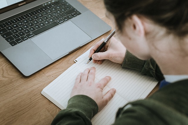 student sitting and working on computer with notebook