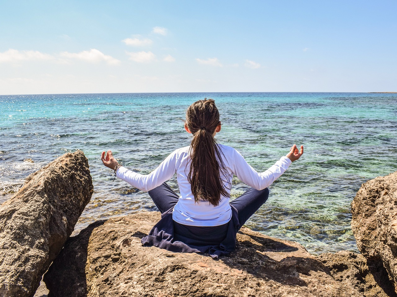 girl and ocean girl with legs crossed and arms out looking out at ocean
